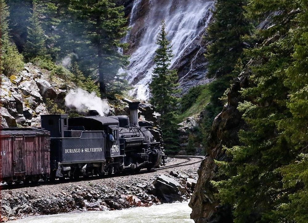 A black train rolls along the tracks in the beautiful Colorado scenery as part of a tour for Durango & Silverton Narrow Gauge Railroad, one of the best weekend getaways near Denver for families.