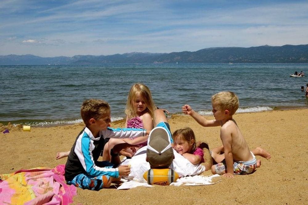 Four kids sit with an adult while they play on the beach near Lake Tahoe.