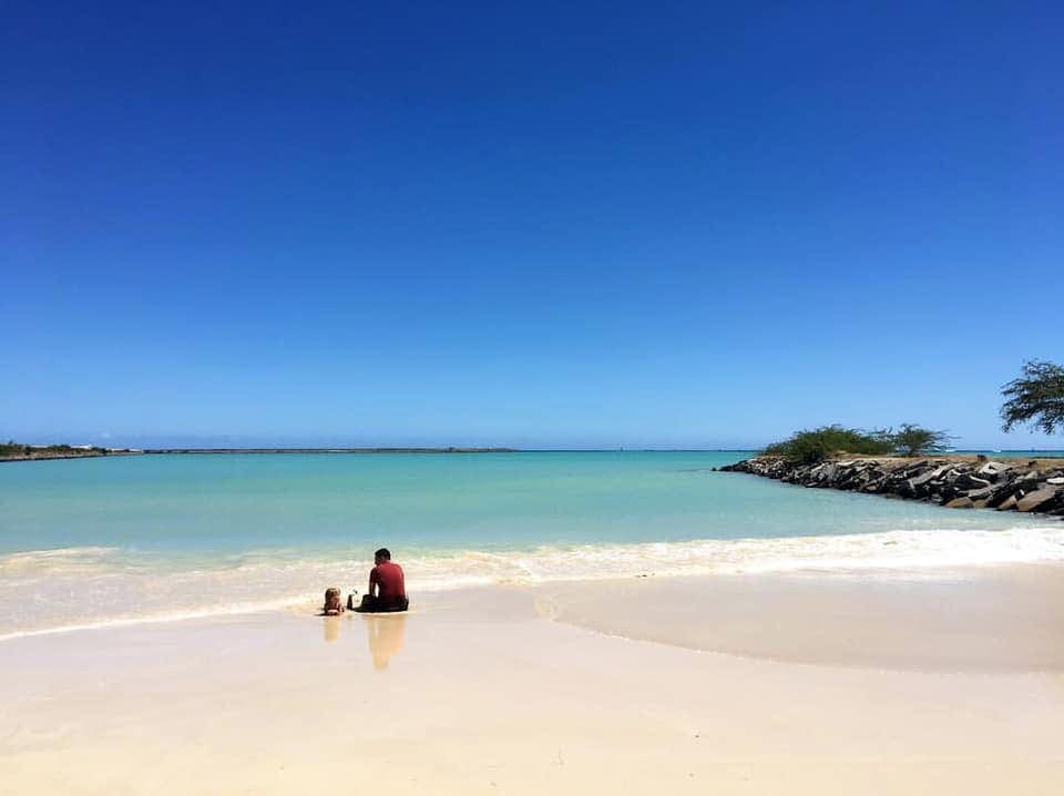 A young boy and his dad sit on a vast, empty beach in O'ahu, one of the top places in travel in 2023 with kids.