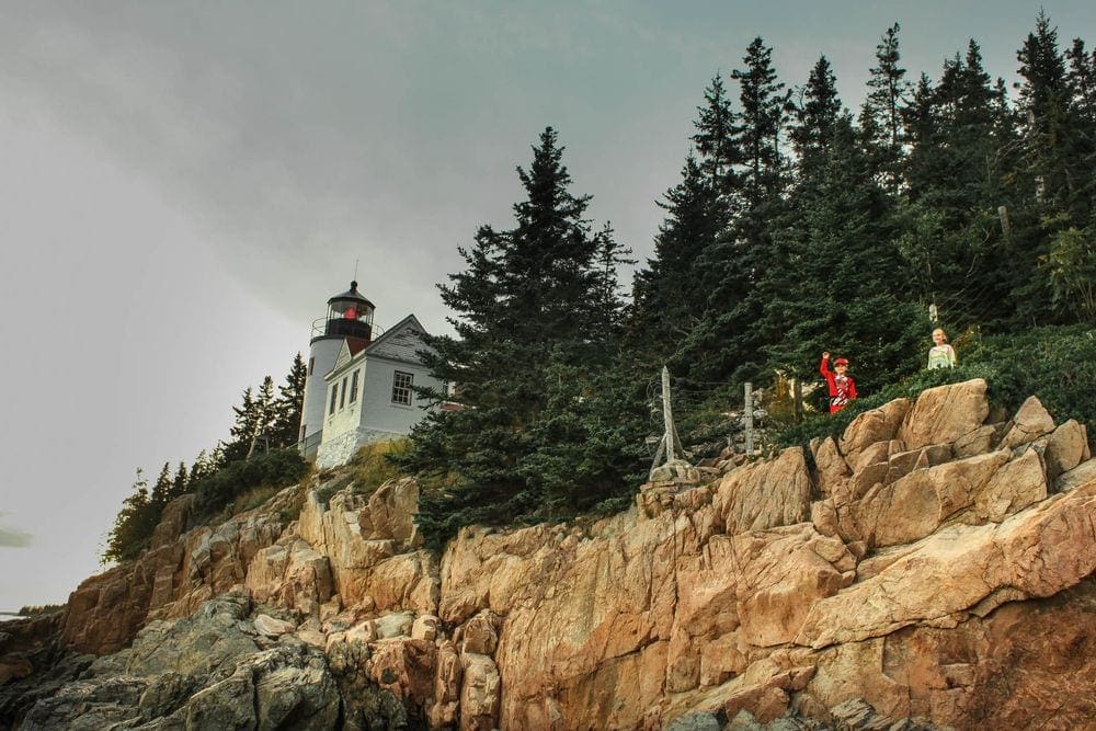 Two kids wave overhead with the Bass Head Lighthouse in the background, one of the bes things to do in Bar Harbor with kids.