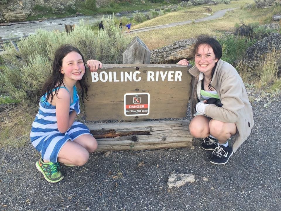 A mother and daughter posing by the Boiling River sign in Yellowstone National Park. 