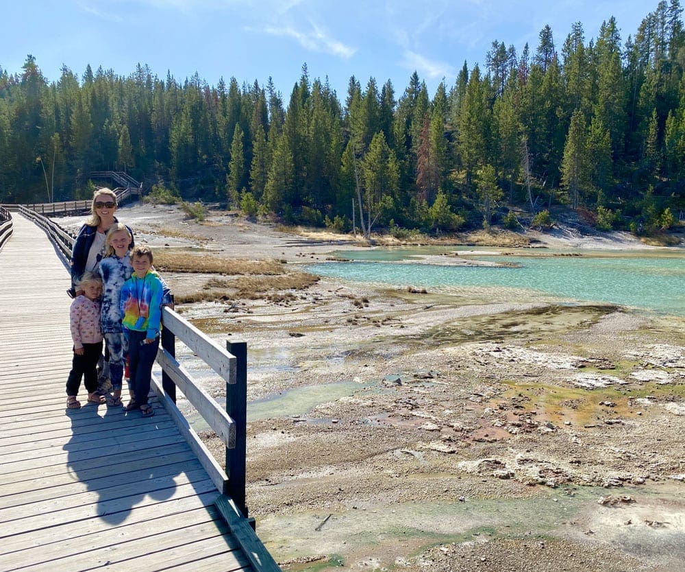 A mom stands with her kids along a boardwalk in Yellowstone National Park.