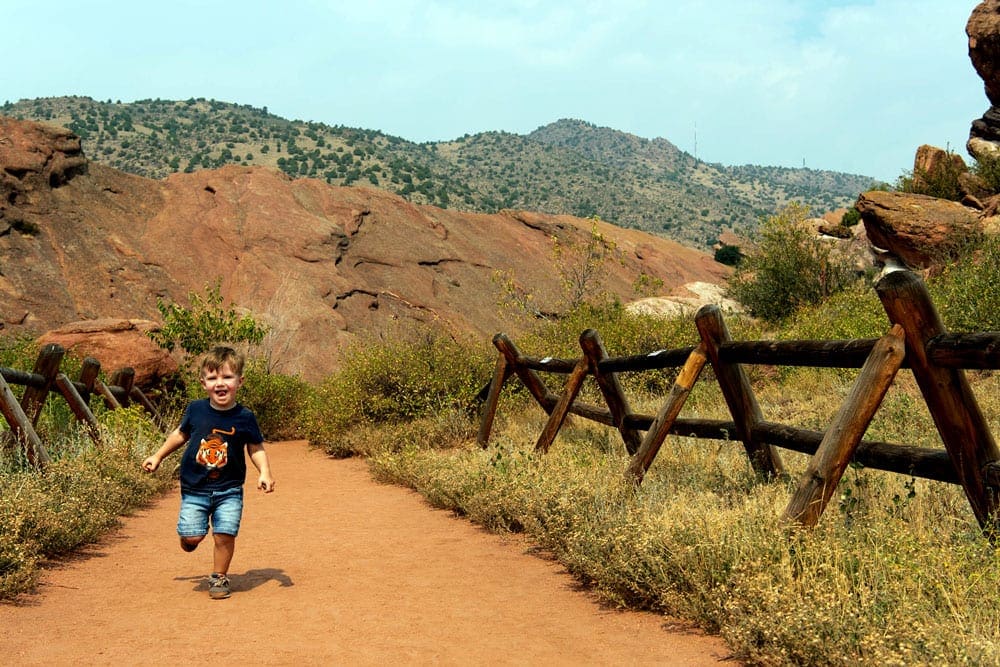 A young boy runs along a dusty path, while hiking in Red Rocks Park in Colorado, one of the best places to visit on a Denver itinerary for families!