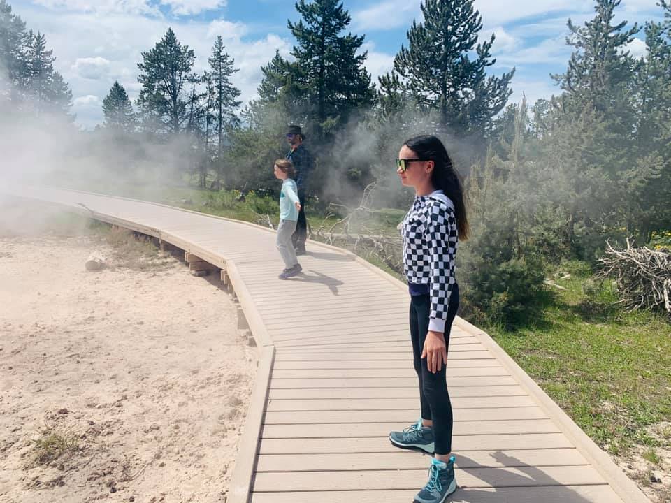 Two kids stand with outstretched arms with their parent while exploring a windy boardwalk in Yellowstone National Park.