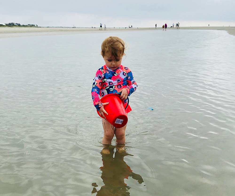 A young girl with a bright red sand pail plays off the shore from Sullivan Island.