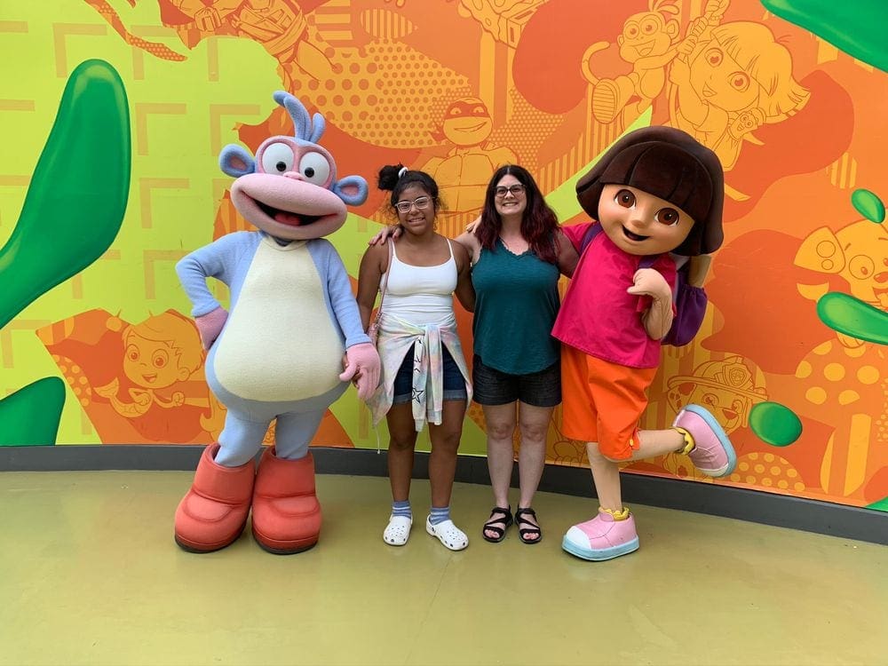 Mom and daughter stand with two characters, Dora the Explorer and Boots, at Nickelodeon Universe in the Mall of America, one of the best places to visit with your young daughter in America.