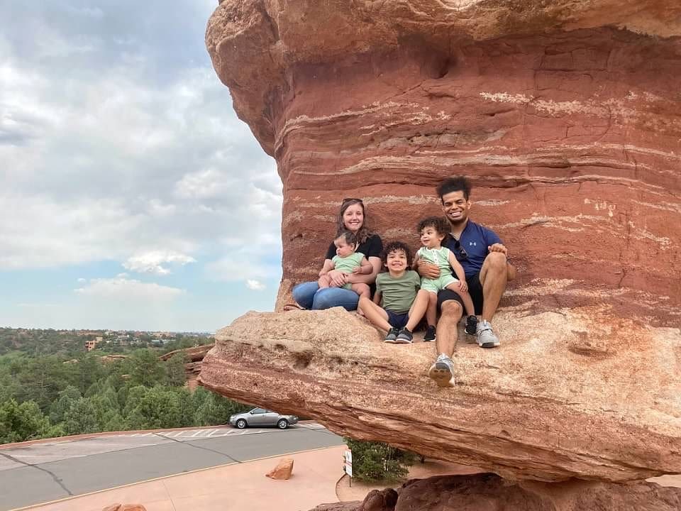 A family of five sits together smiling, tucked into a rock ledge while exploring Garden of the Gods, one of the best things to do in Colorado Springs with kids.