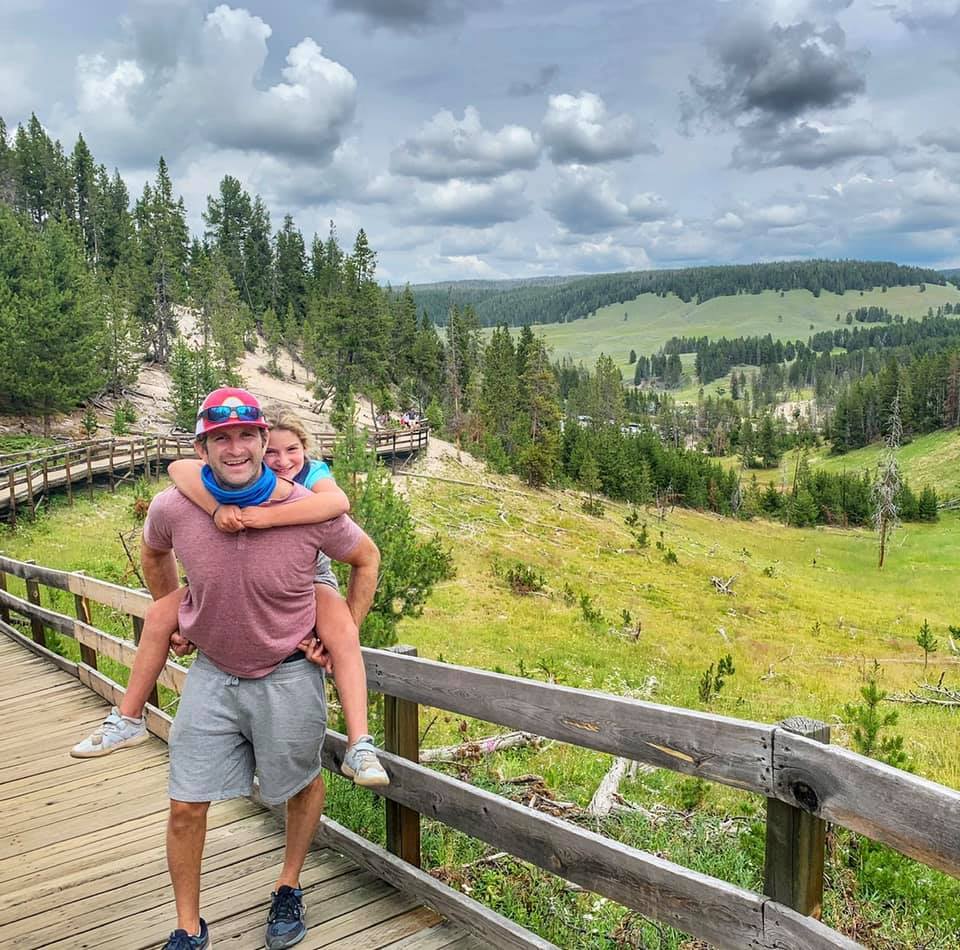 A young girl on her dad's shoulders on the boardwalk in Yellowstone National Park during an itinerary for families.