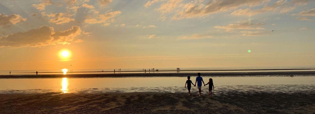 A family of three walks along a beach at sunset in Cape Cod, one of the best East Coast summer destinations for families.