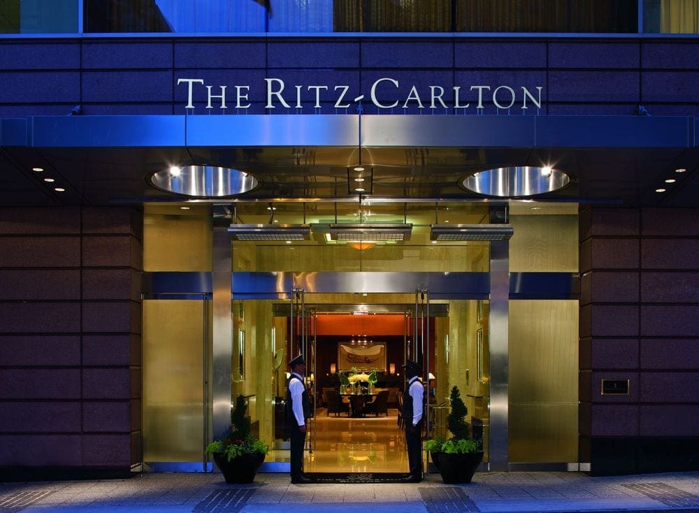 Two gentries stand to open the doors at the The Ritz-Carlton, Boston at night.