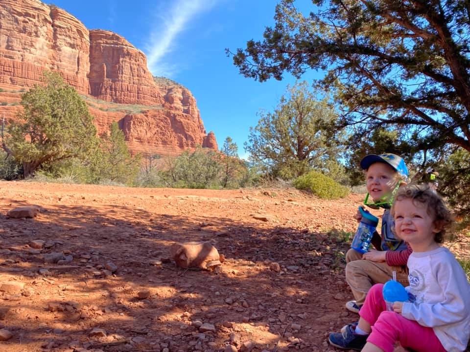 Two kids sit together in the shade, with Sedona's iconic red rocks in the distance, one of the best Thanksgiving destinations in the United States for families.