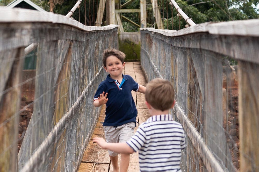 Two brothers run toward eachother on the Hanapepe Swinging Bridge, one of the best things to do in Kauai with kids.