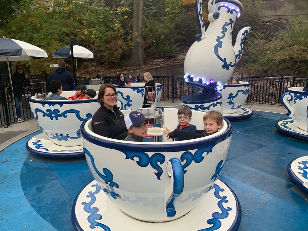 A mom and three young boys sit inside a tea-cup while enjoying the rides at Hershey Park, one of the best places to stop on an NYC to Miami itinerary! 