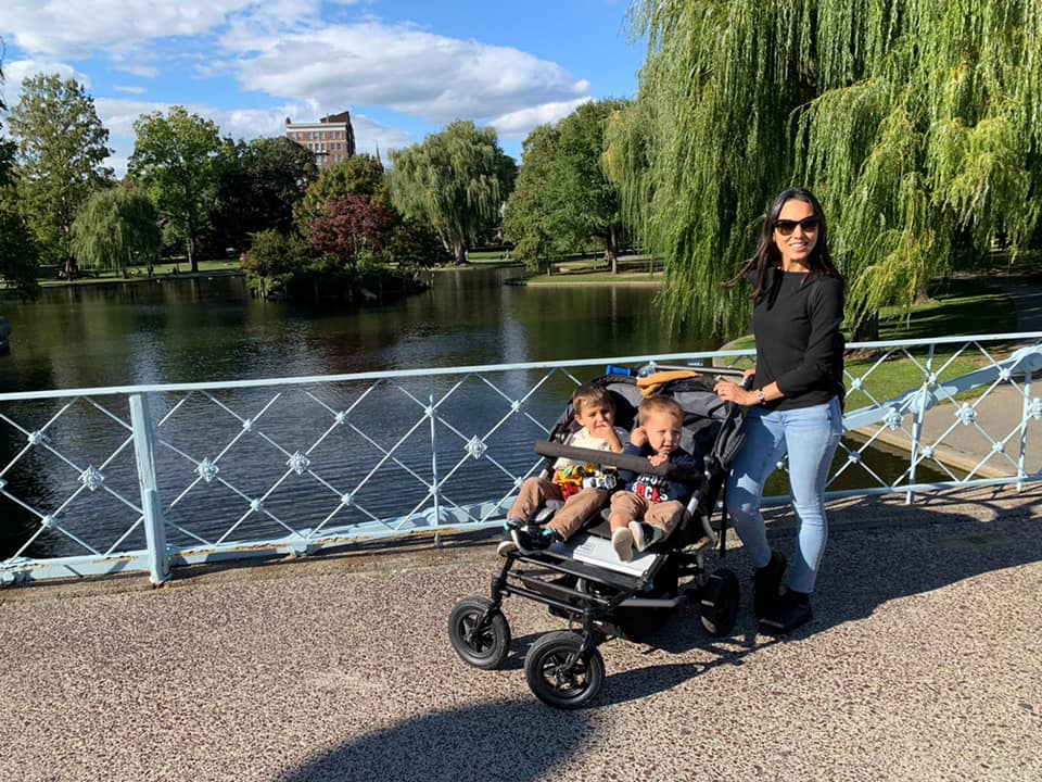 A mom pushes her two kids in a stroller while meanders a Boston park. Boston is one of the best places to visit on a Northeast road trip with kids. 