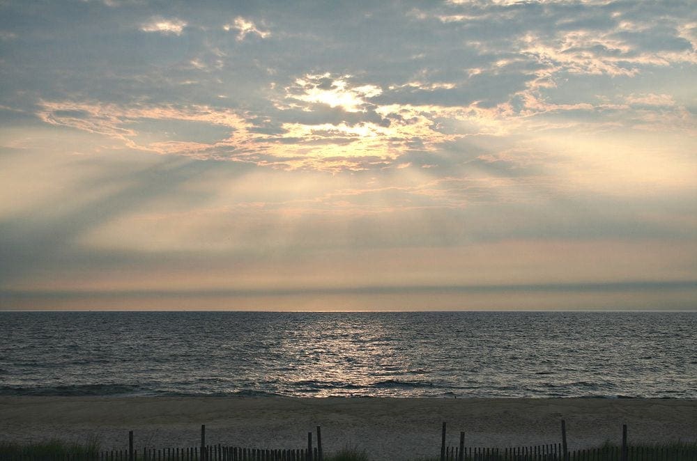 A view of Bethany Beach at sunset, featuring lovely yellow colors and clouds.