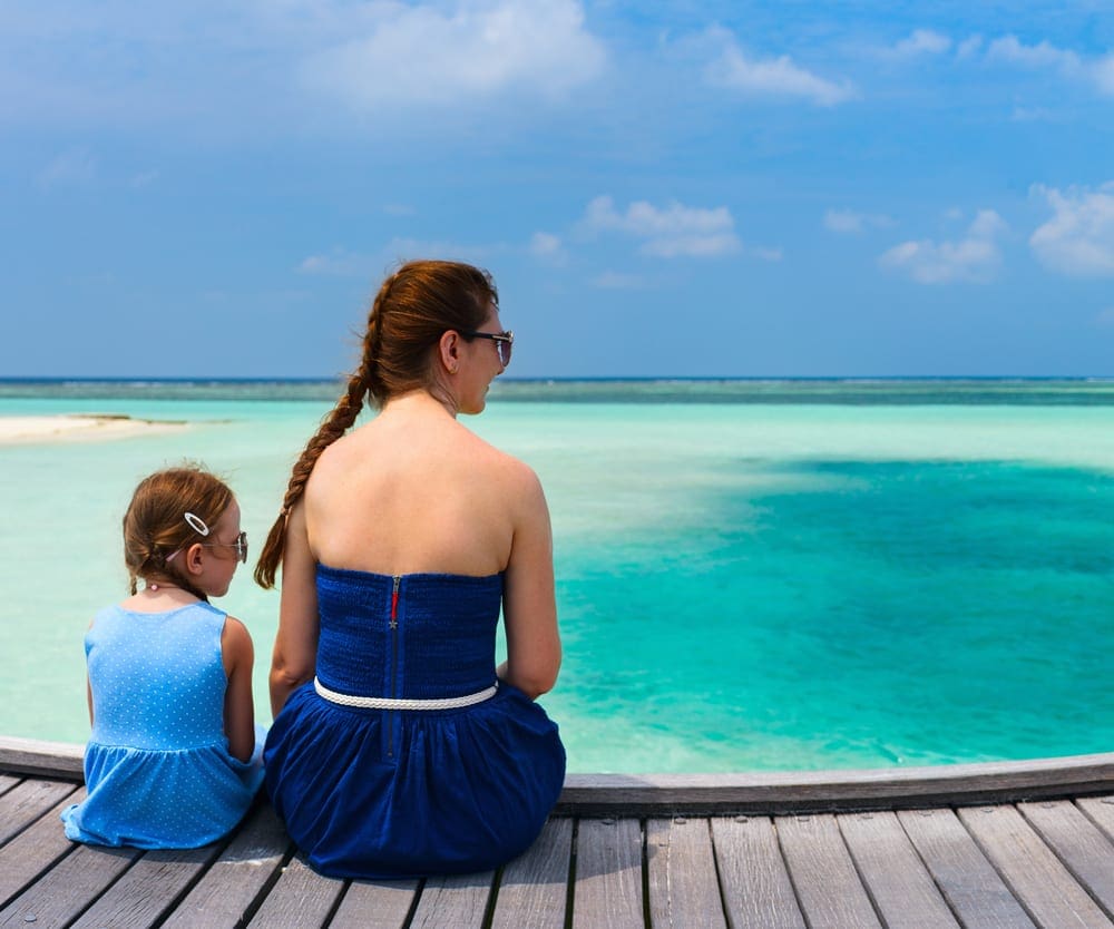 Mom and daughter sitting on a wooden dock looking at the beautiful ocean in the Maldives, one of the best hot places to visit in December for families.