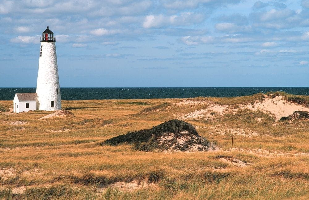 The Great Point Lighthouse rises above coasta grasses with the ocean behind it, it's a great stop on at family vacation to Nantucket.
