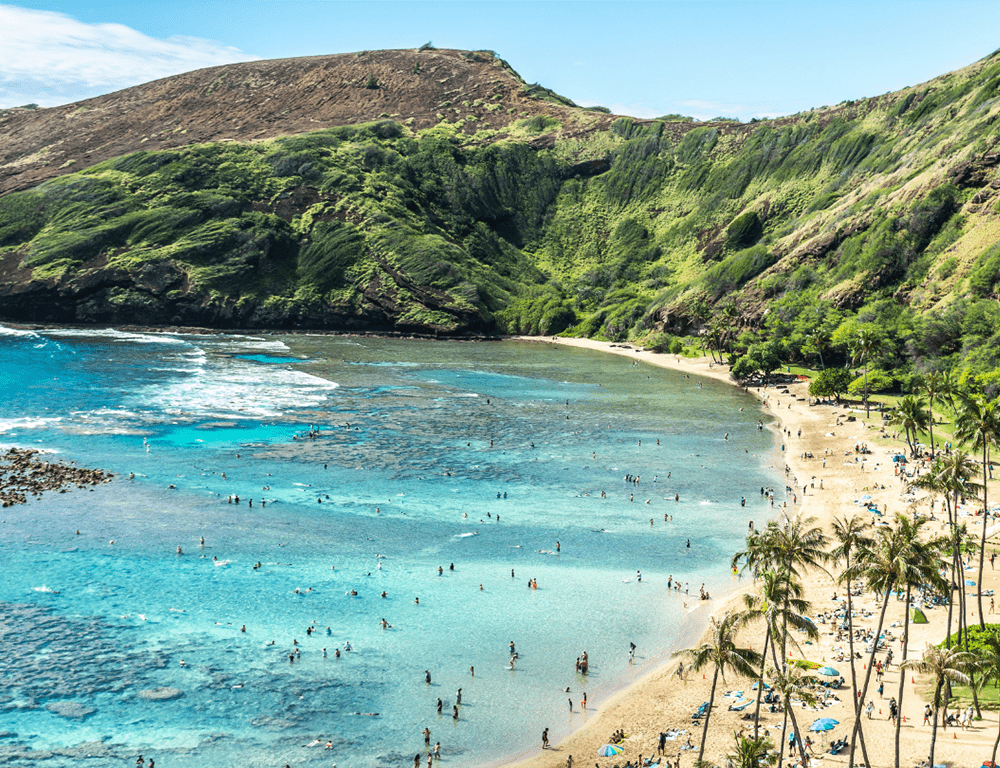 A long stretch of Hanauma Bay, dotted with beach goers, on a sunny day.