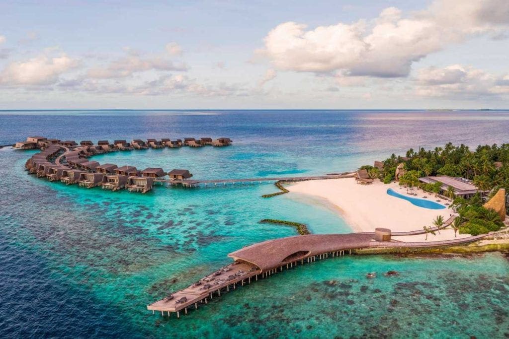 An aerial view of the St. Regis Maldives Vommuli Resort, featuring over-water bungalows and a pristine beach.