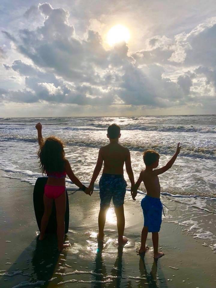 Three kids stand hand-in-hand looking at a gorgeous sunset on St. Simmons Island.