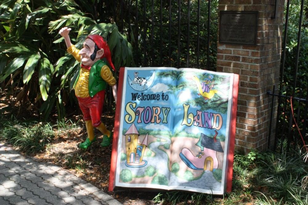 A gnome statue stands near a large statue of a book reading "Weclome to Story Land".
