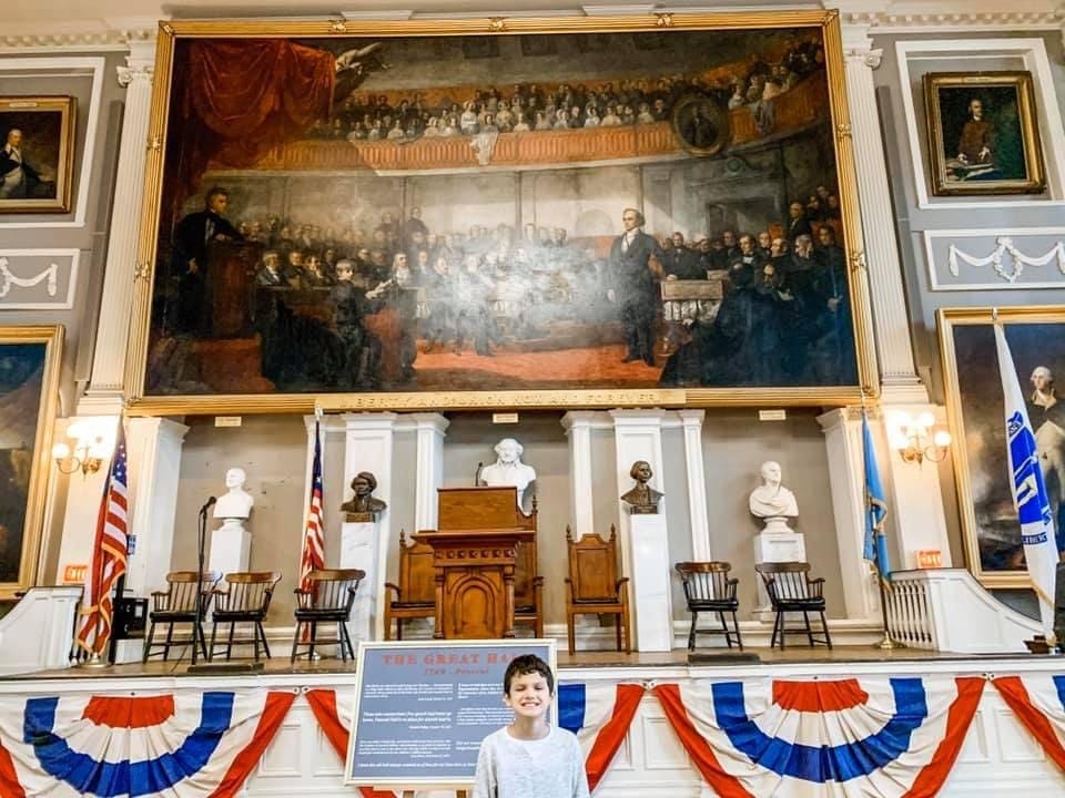 A young boy smiles while standing in front of an exhibit at the Faneuil Hall Marketplace.