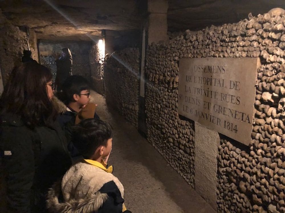 A mom and her two kids stand together looking at an ancient wall within one of the Paris catacombs.