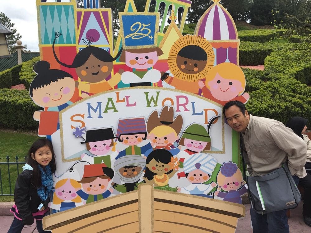 A dad and his daughter pose near the 'Small World' sign at Disneyland Paris, one of the best places to visit in France with kids.