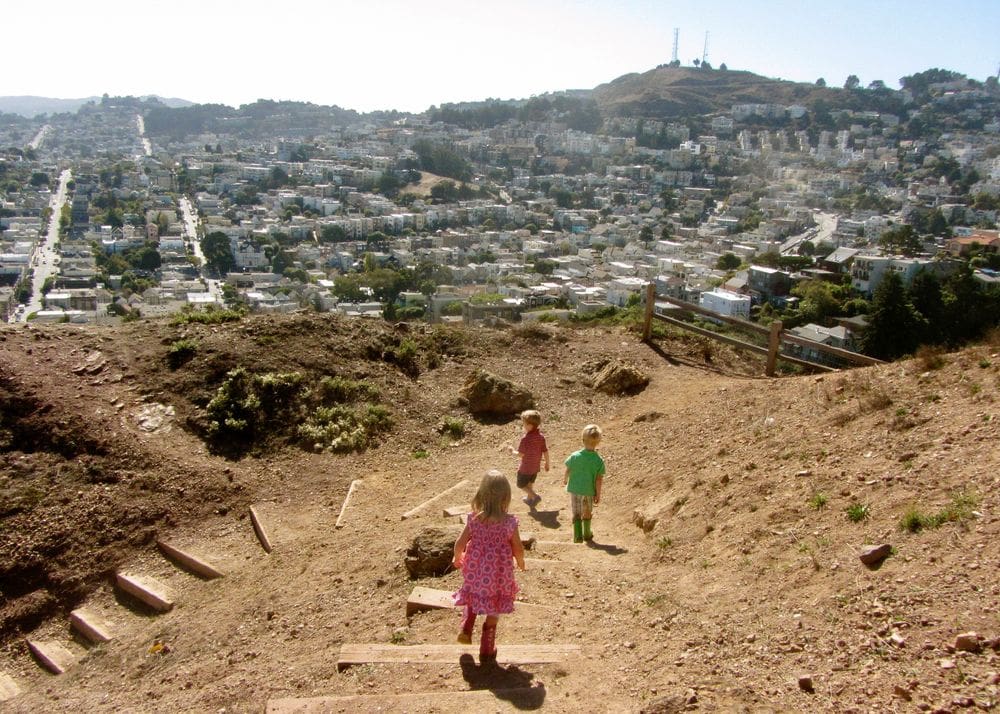 Three young toddlers walk down a slight hill while hiking the Cross Town Trail.
