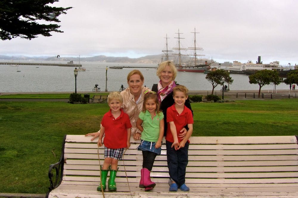 A mom, grandma, and three toddlers pose together with the Fisherman's Wharf in the distance, one of the best things to do in San Francisco with kids.