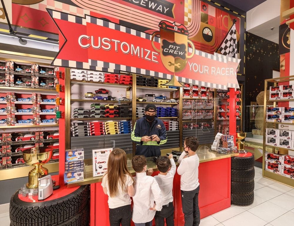 Four kids watch a staff member make a customized race car for kids at FAO Schwarz, one of the best things to do New York City with young kids.