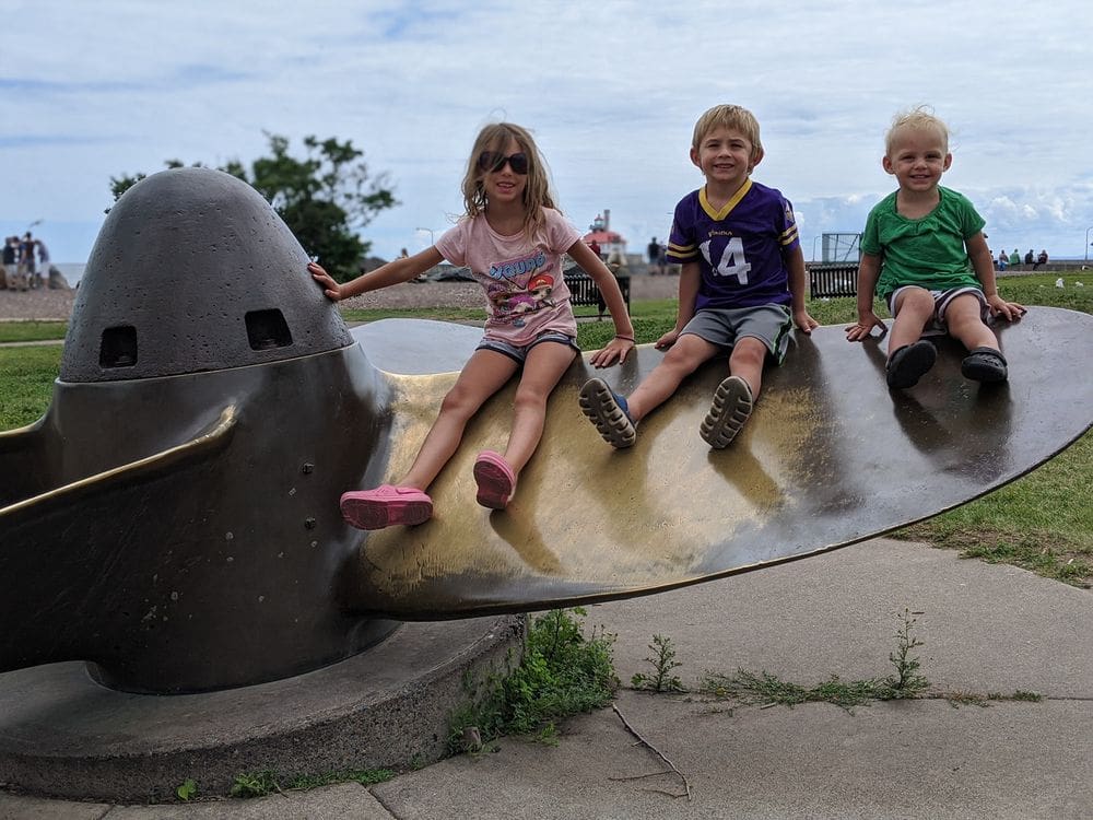 Three kids sit on a large boat propeller that is now an art installation in Canal Park in Duluth, Minnesota, one of the weekend getaways from Minneapolis for families.