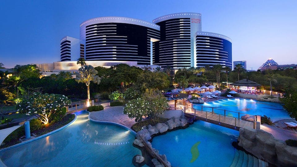 A view of the Grand Hyatt Hotel and Residences Dubai, featuring its many pools at night at one of the best places to stay in the UAE with kids.