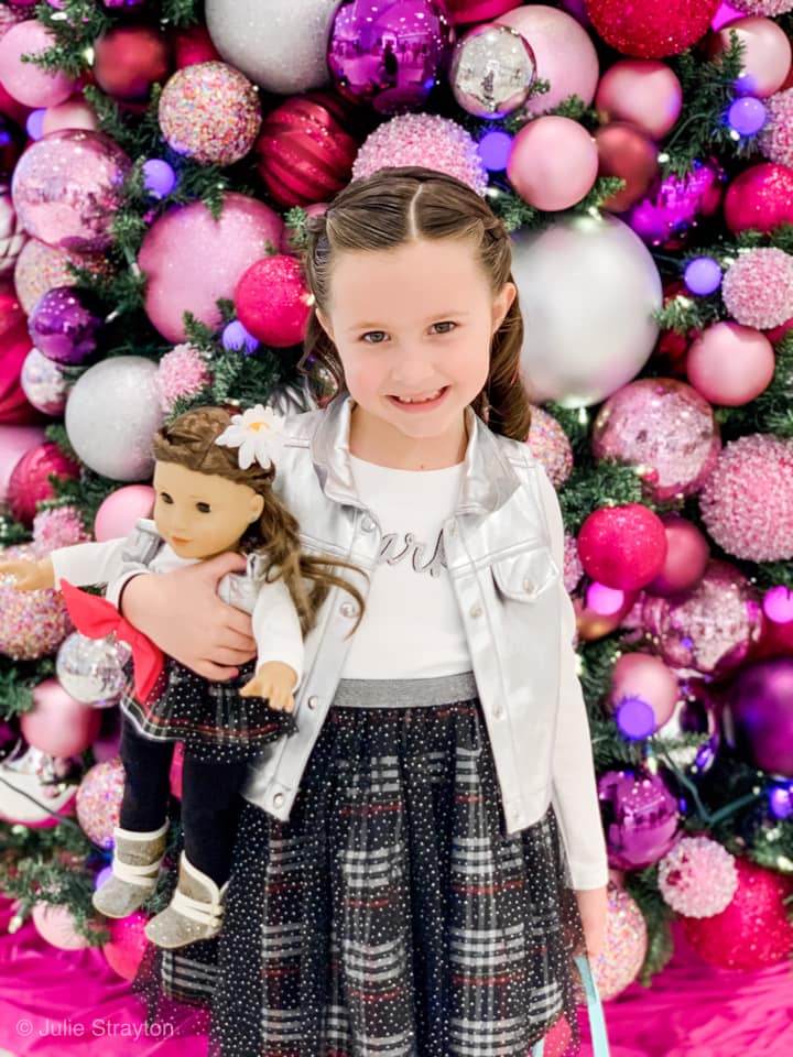 A young girl stands with her American Doll in a Christmas display at the American Girl Doll Store.