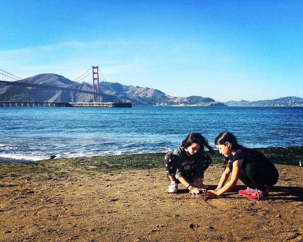 Two girls play in the sand with San Francisco Bay in the background, one of the top places in travel in 2023 with kids.