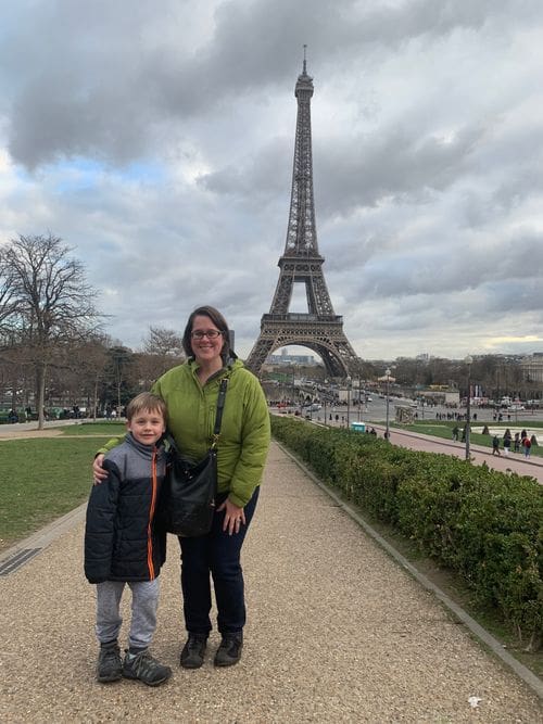 A mom and her young son stand together with the Eiffel Tower standing proudly in the distance.
