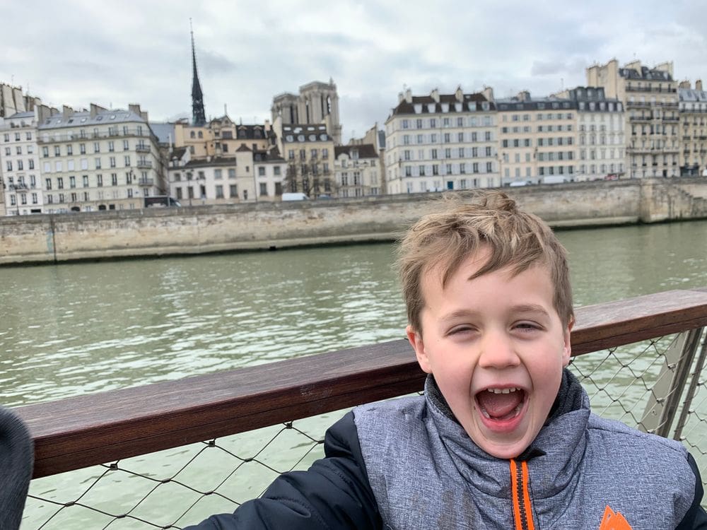 A young boy smiles broadly while enjoy a boat cruise down the Seine River.