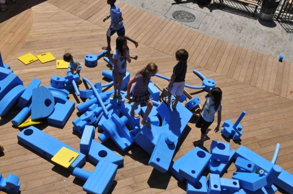 Six kids play amongst several large blue foam pieces at the Imagination Playground, one of the best things to do New York City with young kids.
