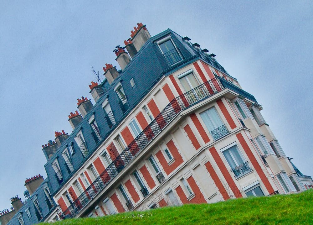 A view of the famous Paris sinking house on the other side of bright green grass.