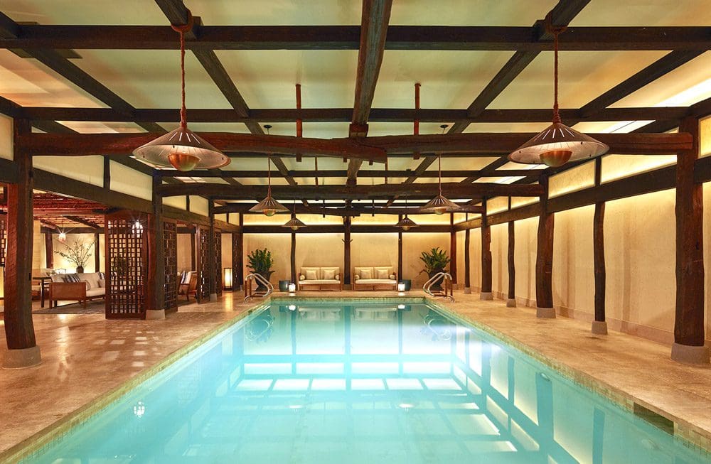 A view of the indoor pool at the The Greenwich Hotel, with nearby loungers and well-designed space featuring wood beams, knowing where to stay is an important piece of knowing all about New York City with kids.