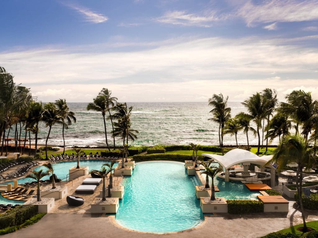 Center view of the outdoor pool surrounded by palm trees at the Caribe Hilton, one of the best family resorts in Puerto Rico. 