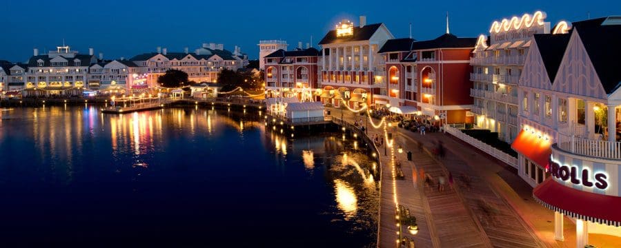 THe Disney’s Boardwalk Resort  at night, lit up with lights shimmering on the water.