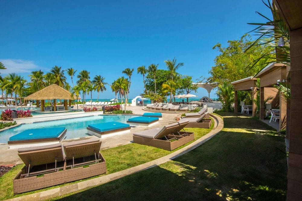 Picture of one of the Fairmont El San Juan Hotel's four outdoor pools, surrounded by lush palm trees and lounge chairs. It's one of the best family resorts in Puerto Rico. 