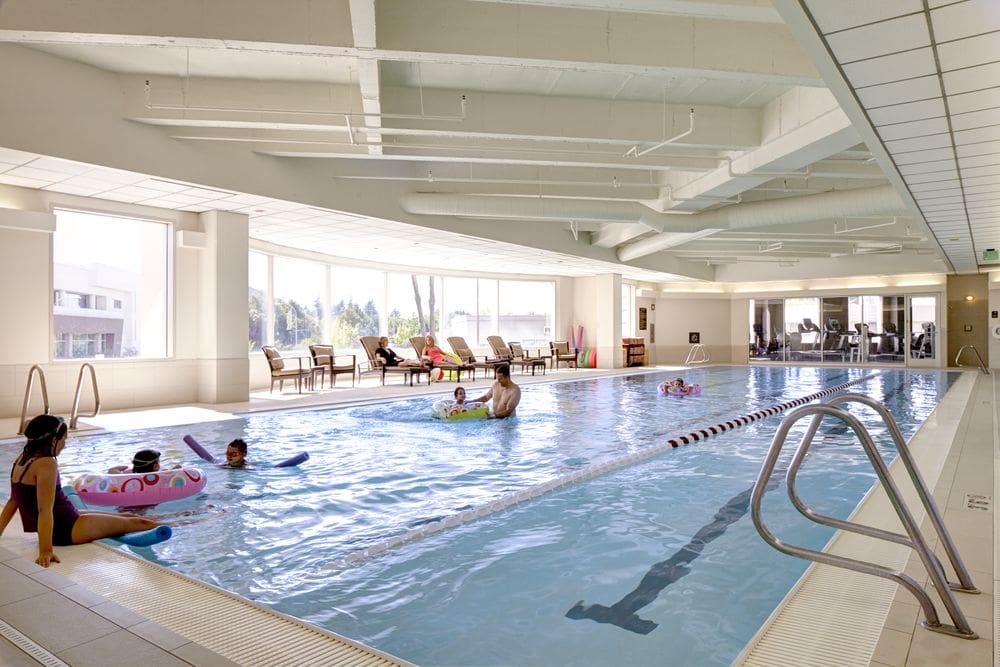 Two parents play with their four kids in the pool, while two woman sit in poolside loungers, at the natural-lit pool in the Hyatt Regency Bellevue On Seattle's Eastside.