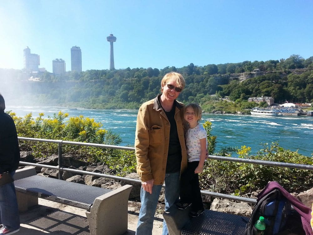 A dad and his daughter smile together above Niagara Falls with the Ontario skyline in the distance, one of the best Labor Day Weekend getaways near NYC with kids.