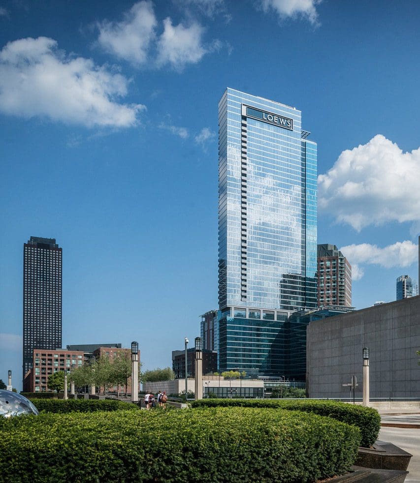 A view of the Loews Chicago Hotel, across a green space and surrounded by other buildings on a sunny day.