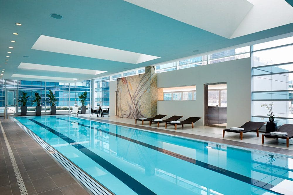 Indoor lap pool inside the fitness center at the Loews Chicago Hotel, surrounded by plants and brown lounge chairs.