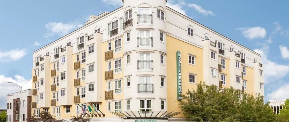 The yellow exterior to the Mediterranean Inn, featuring several windows, on a sunny day.