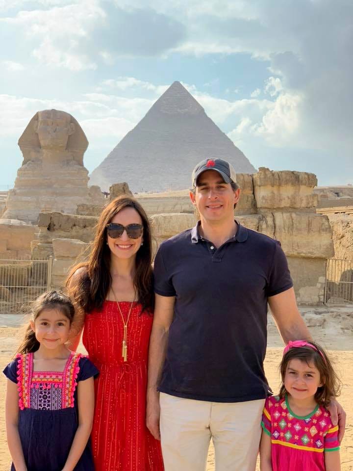 A family of four stands together, Great Sphinx of Giza and a pyramid can be seen in the distance.