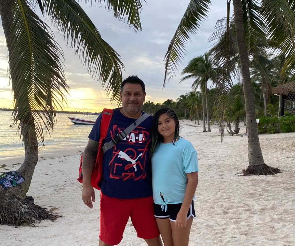 A dad and his daughter stand together on a beach in Akumal.